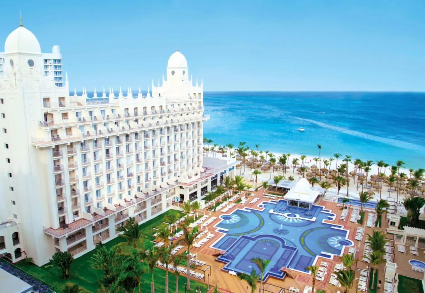 Aerial view of Hotel Riu Palace Aruba towers, pools, palms, beach, and ocean.