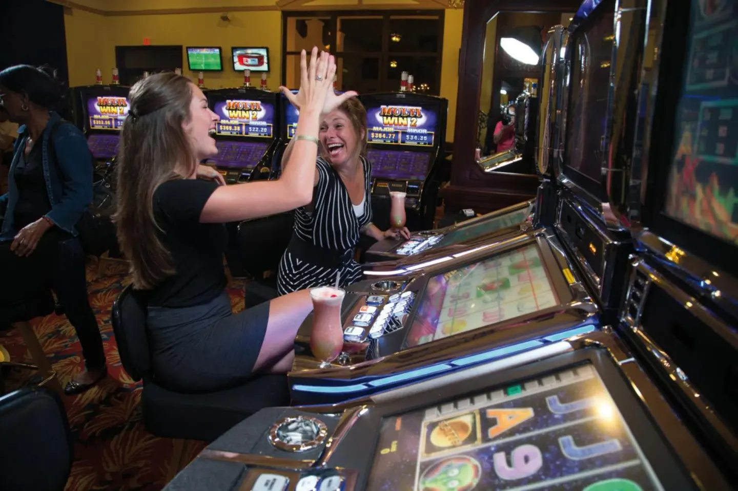Guests high-five beside slot machines at Hotel Riu Palace Aruba.
