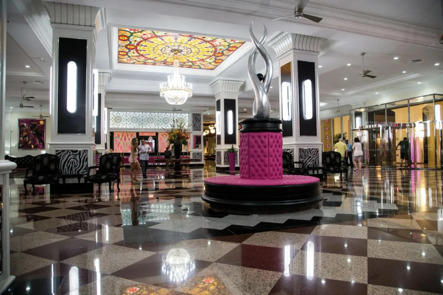 Lobby seating and silver sculpture beneath a stained-glass ceiling at Hotel Riu Palace Aruba.