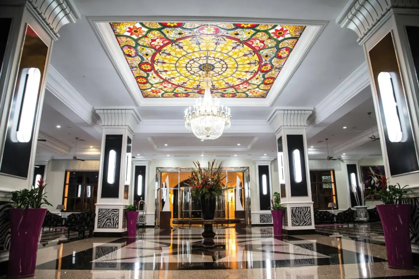 Lobby ceiling with stained-glass panel and chandelier at Hotel Riu Palace Aruba.