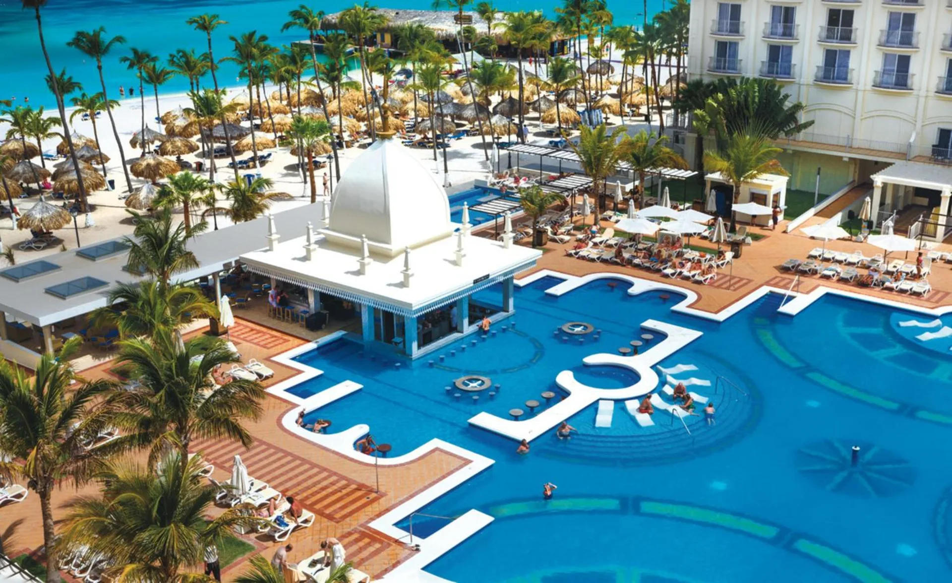 Aerial view of the pool, beach, palms, and resort buildings at Hotel Riu Palace Aruba.