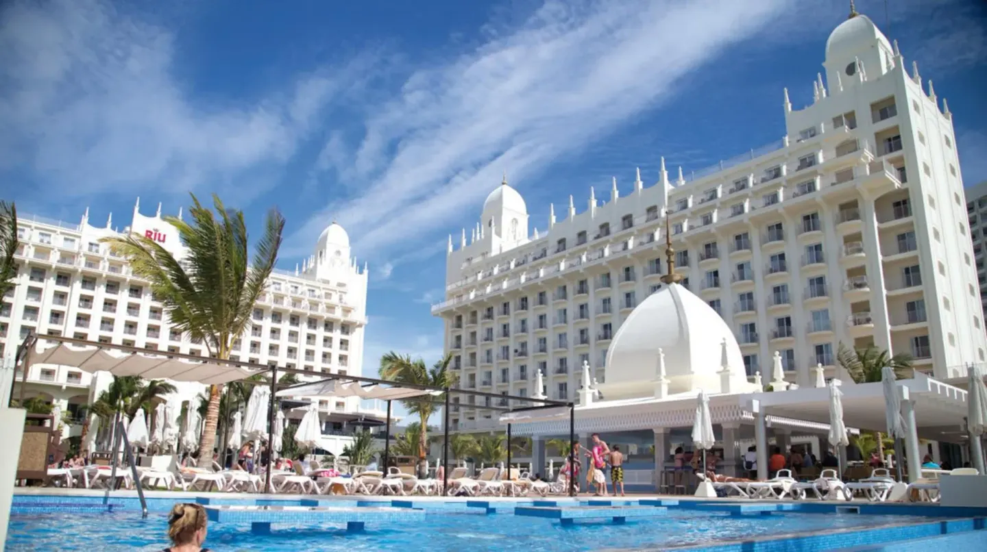 Pool deck and white resort buildings at Hotel Riu Palace Aruba.