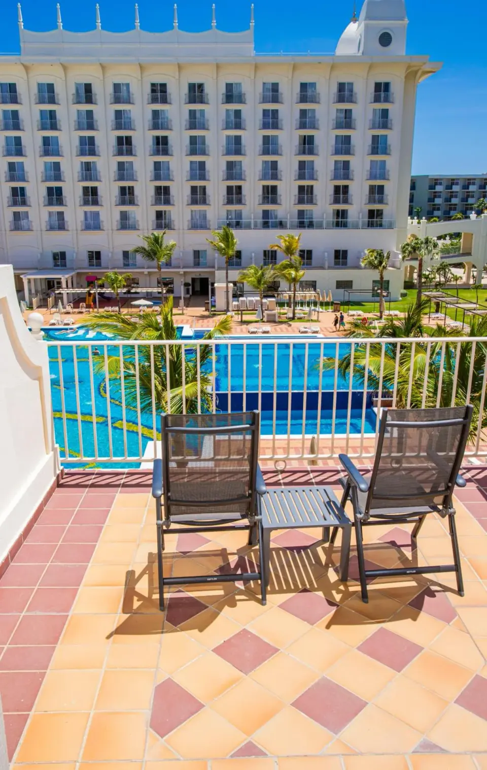 Balcony chairs overlook the pool and resort facade at Hotel Riu Palace Aruba.