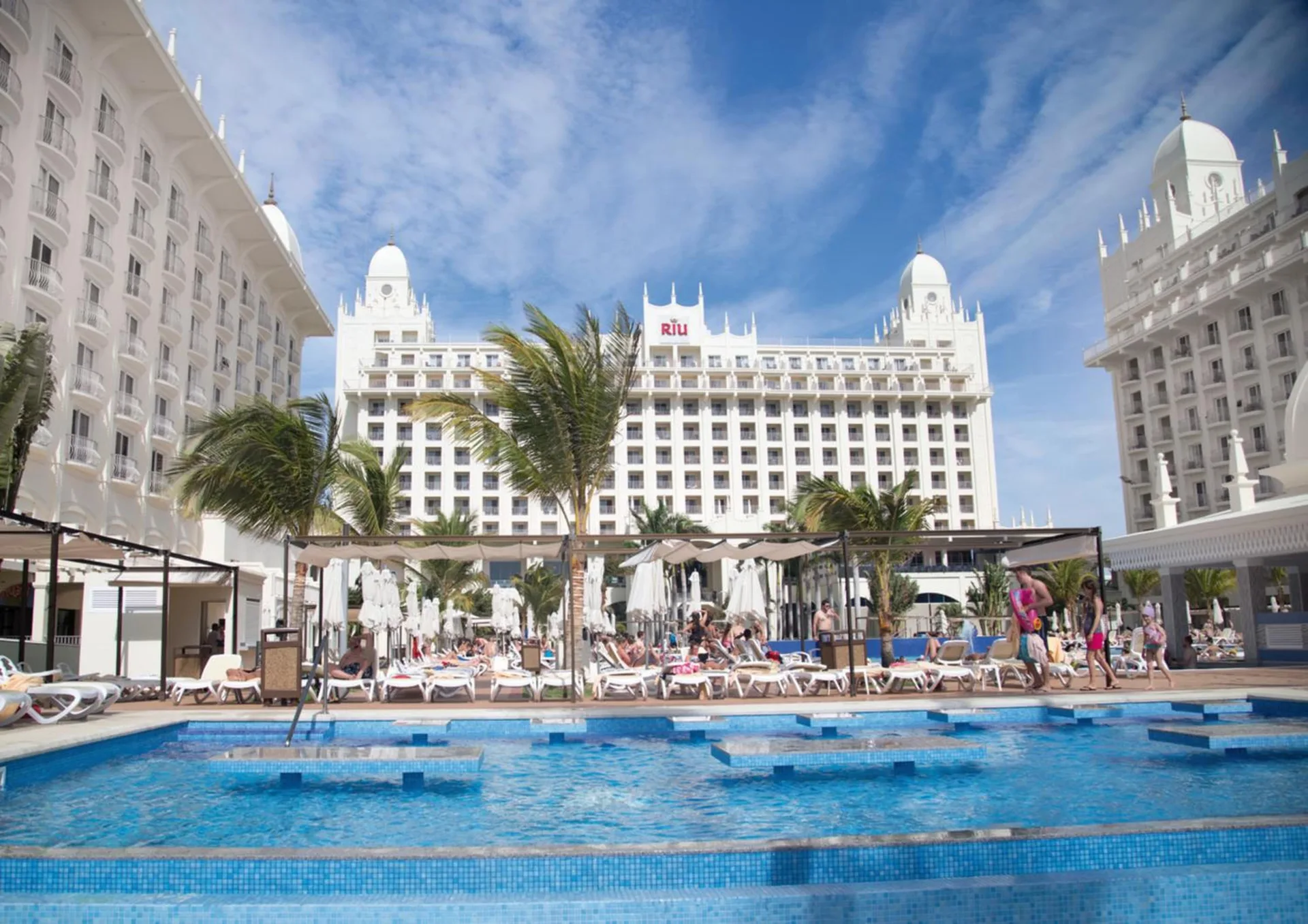 The white resort towers and pool deck are seen under a blue sky at Hotel Riu Palace Aruba.