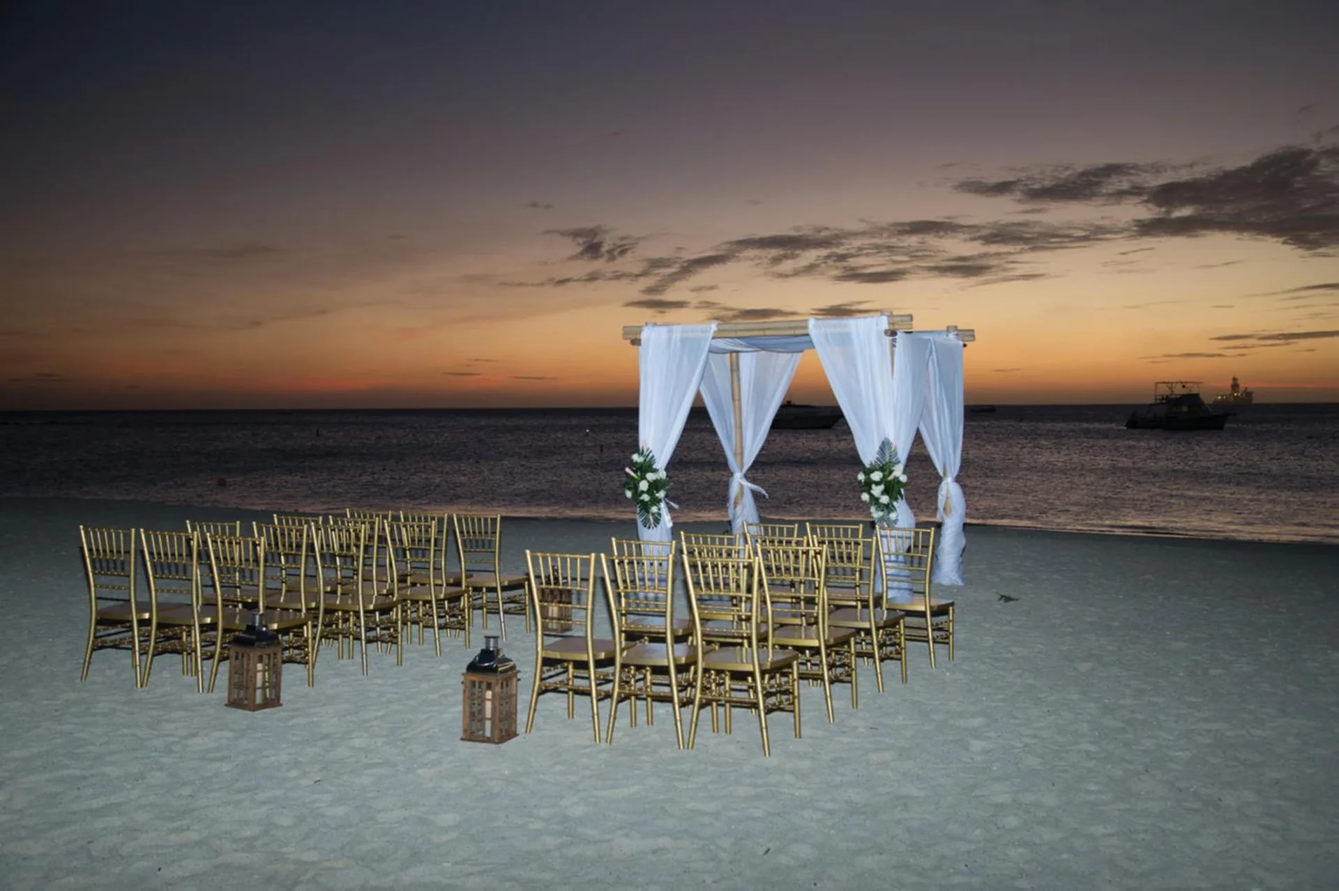 Beach wedding setup with white canopy and gold chairs at Hotel Riu Palace Aruba.