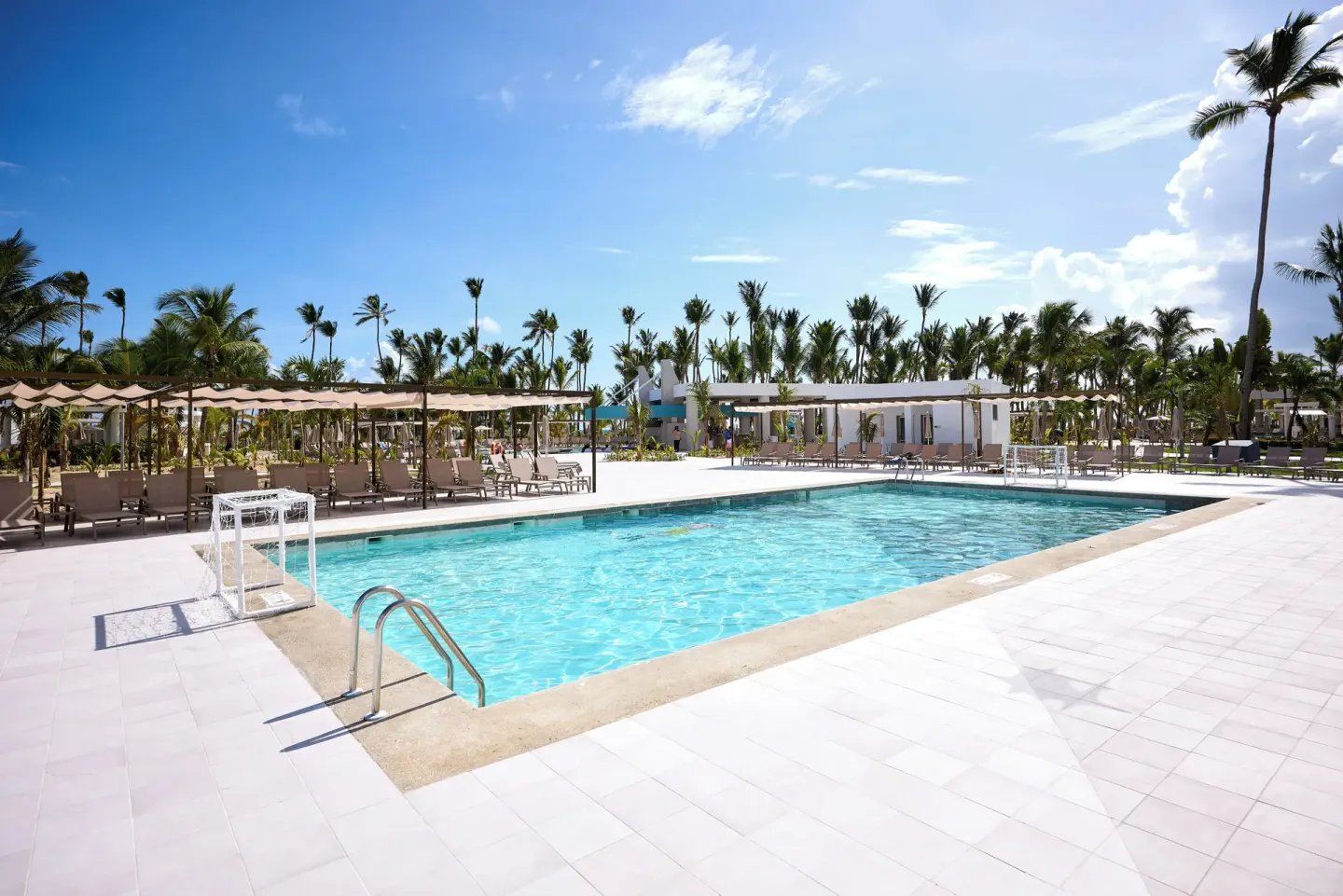 Outdoor pool with loungers and palm trees at Hotel Riu Palace Bavaro.