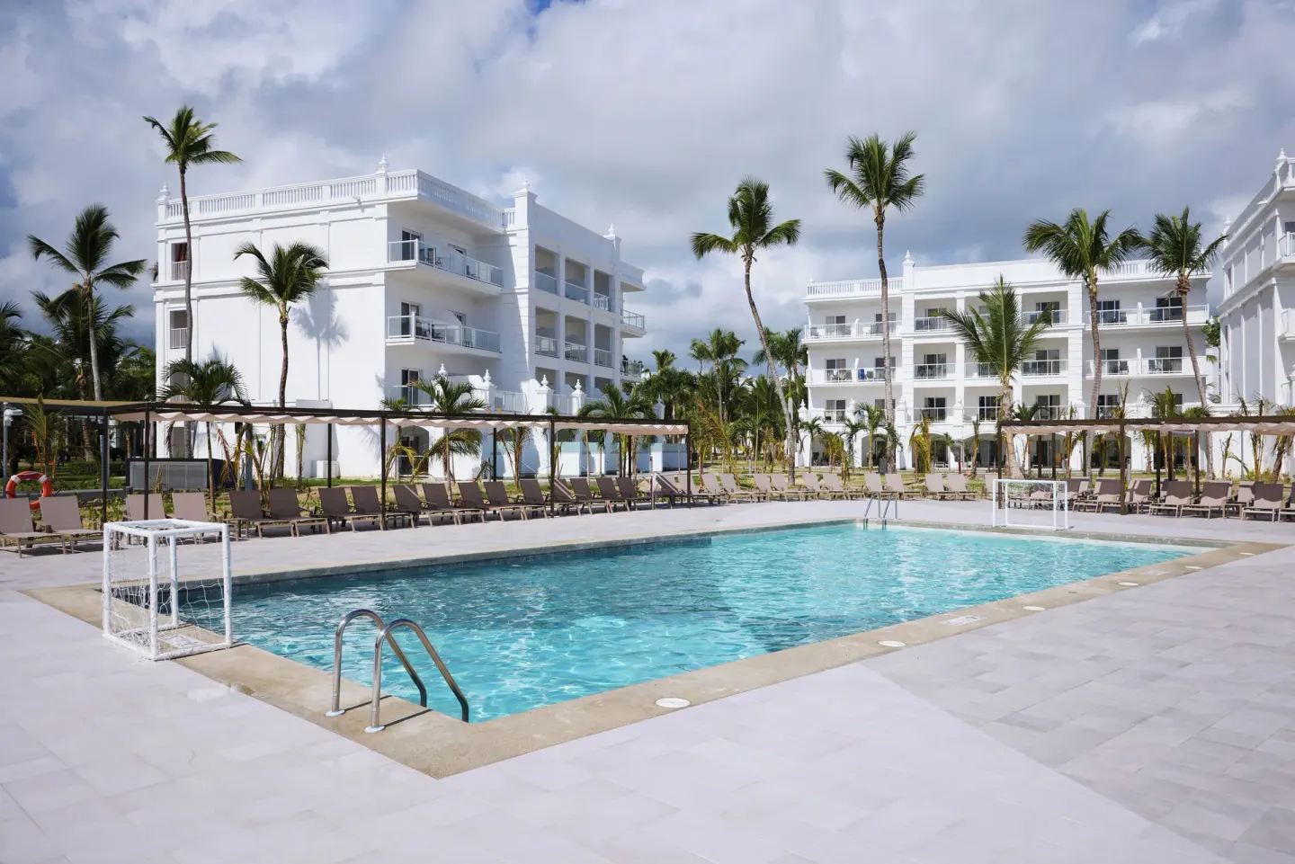 Pool courtyard with white guest buildings and palm trees at Hotel Riu Palace Bavaro.