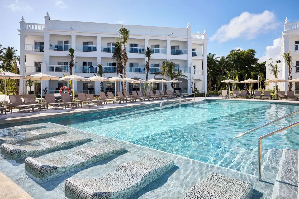 Pool with in-water loungers and white guest buildings at Hotel Riu Palace Bavaro.