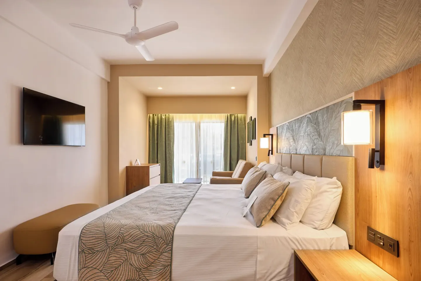 King bed area in a Family Suite at Hotel Riu Palace Bavaro with balcony doors and wall-mounted TV.