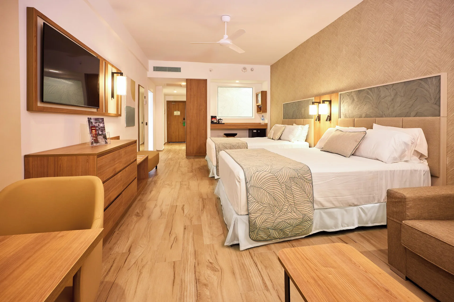 Two-bed bedroom in a Family Suite at Hotel Riu Palace Bavaro with dresser, TV, desk, and seating.