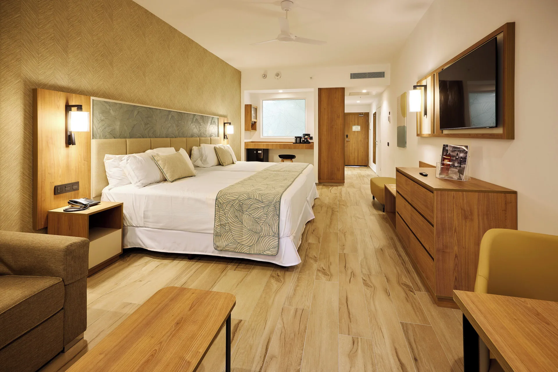 Junior Suite Connecting Rooms bedroom with twin beds, sofa, TV, and dresser at Hotel Riu Palace Bavaro.
