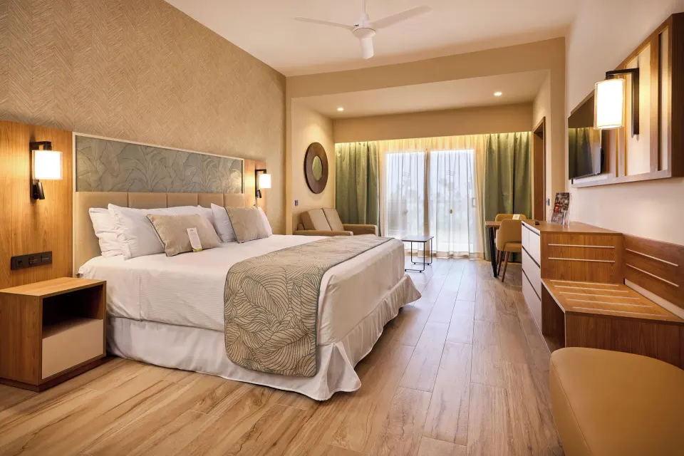 Junior Villa king bed with seating area, desk and balcony doors at Hotel Riu Palace Bavaro.