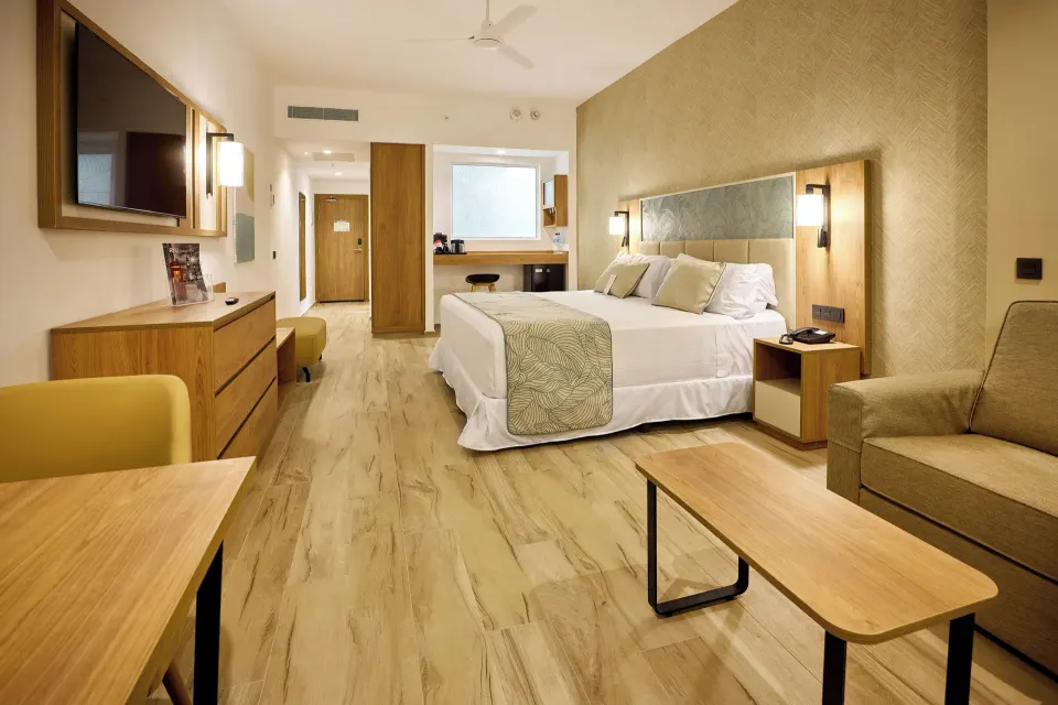 Junior Villa room with king bed, sofa, desk and wall TV at Hotel Riu Palace Bavaro.