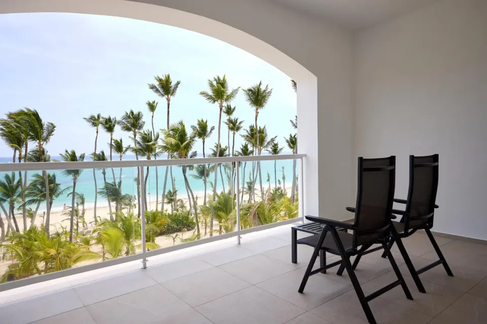 Ocean-view suite balcony with chairs and palm-lined beach at Hotel Riu Palace Bavaro.