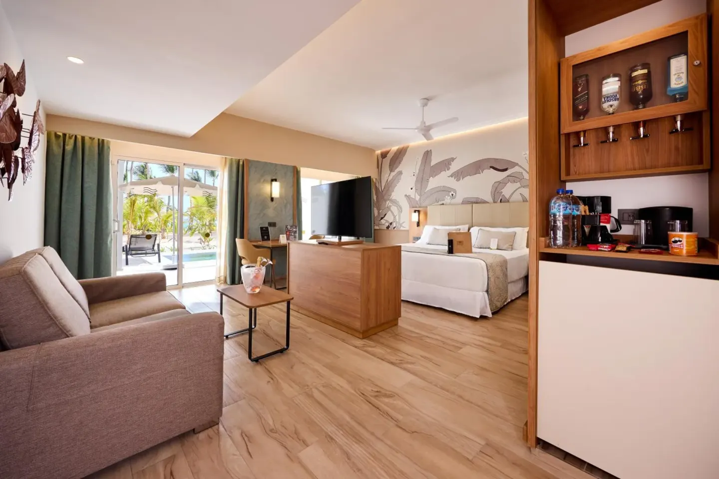 Suite with king bed, sofa, minibar area, and terrace doors at Hotel Riu Palace Bavaro.
