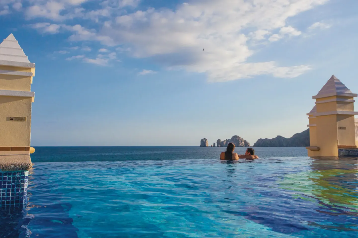Guests in an infinity-edge pool overlooking the ocean at Hotel Riu Palace Cabo San Lucas.