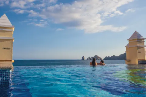 Guests in an infinity-edge pool overlooking the ocean at Hotel Riu Palace Cabo San Lucas.