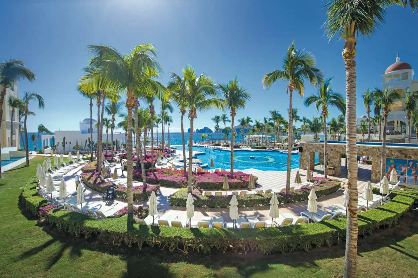 Main pool area with palms and ocean beyond at Hotel Riu Palace Cabo San Lucas.
