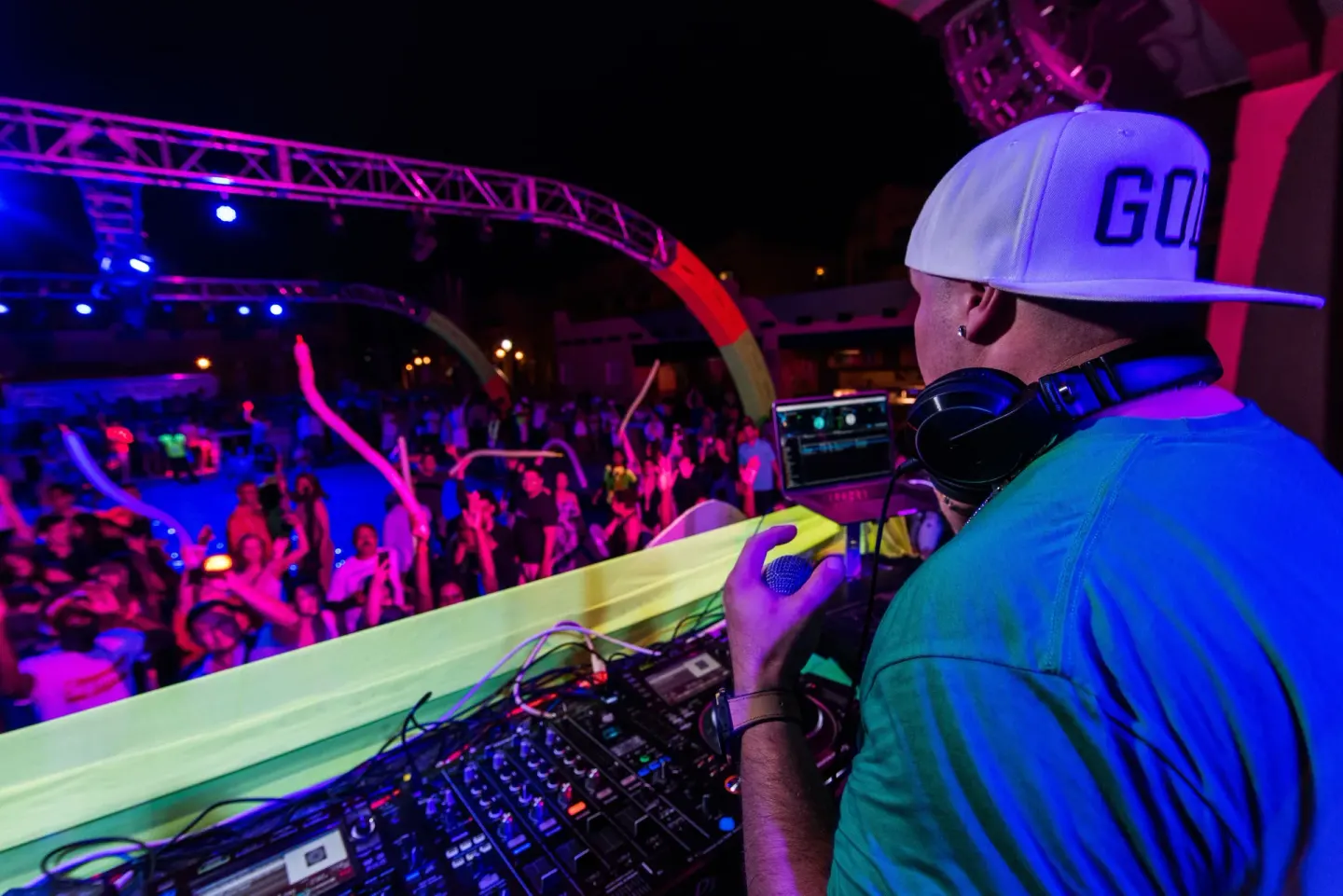 DJ overlooking a neon-lit night party crowd at Hotel Riu Palace Cabo San Lucas.