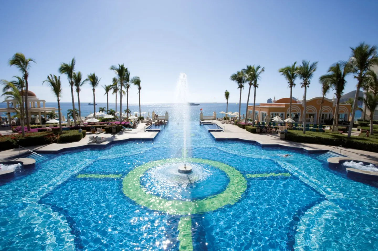 Symmetrical ocean-facing pool with central fountain at Hotel Riu Palace Cabo San Lucas.