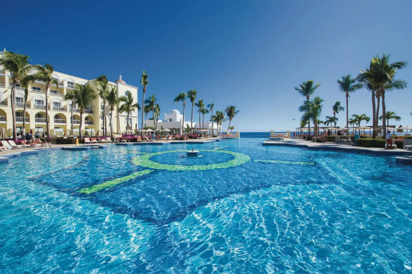 Wide resort pool with palm trees and ocean view at Hotel Riu Palace Cabo San Lucas.