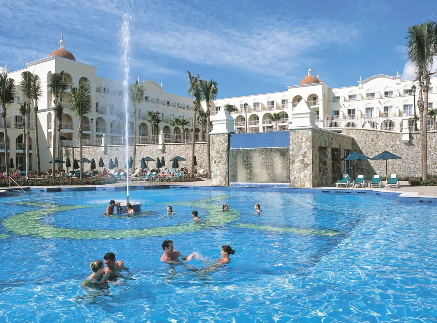Guests swimming near a fountain and waterfall at Hotel Riu Palace Cabo San Lucas.