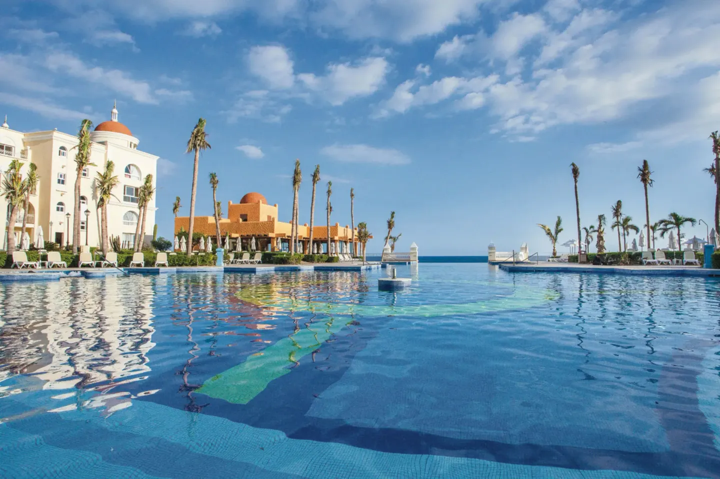 Resort pool reflecting buildings and palms at Hotel Riu Palace Cabo San Lucas.