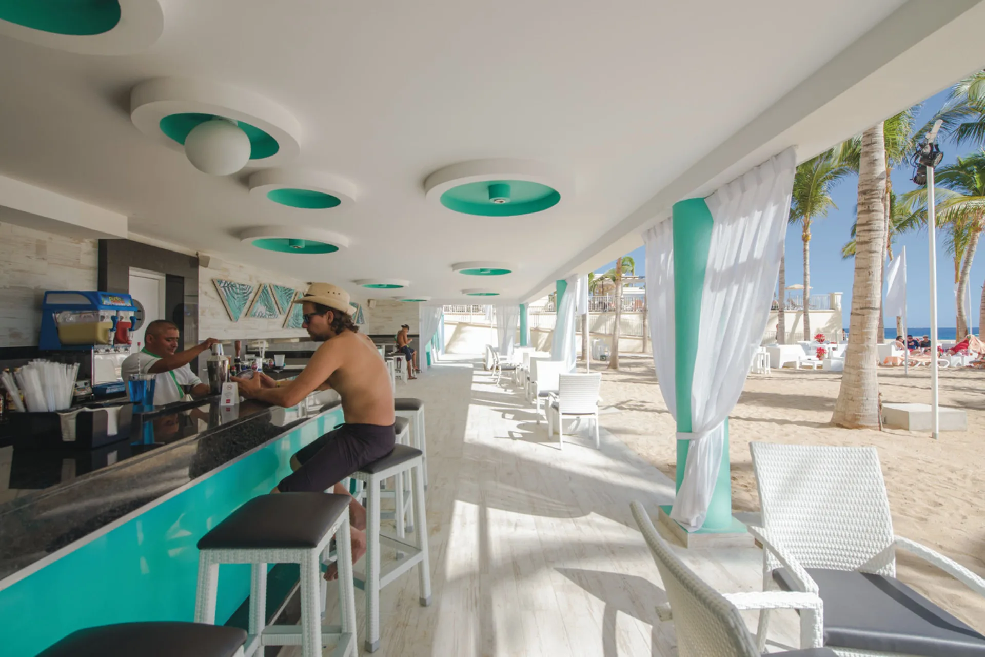 Beach bar with turquoise counter and white seating at Hotel Riu Palace Cabo San Lucas.