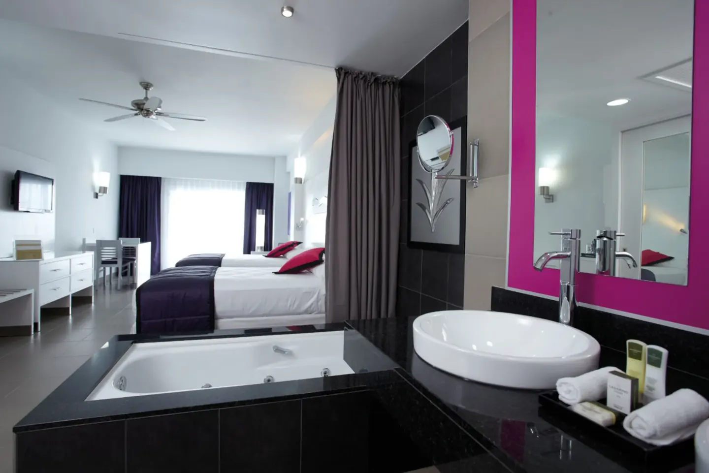 Open-plan guest room bathroom with tub, vanity, and two beds at Hotel Riu Palace Costa Rica.