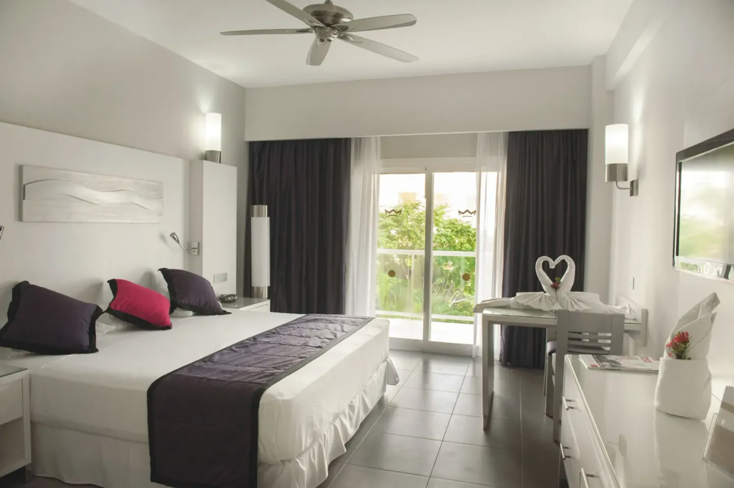 Guest room with king bed, balcony doors, and towel swans at Hotel Riu Palace Costa Rica.