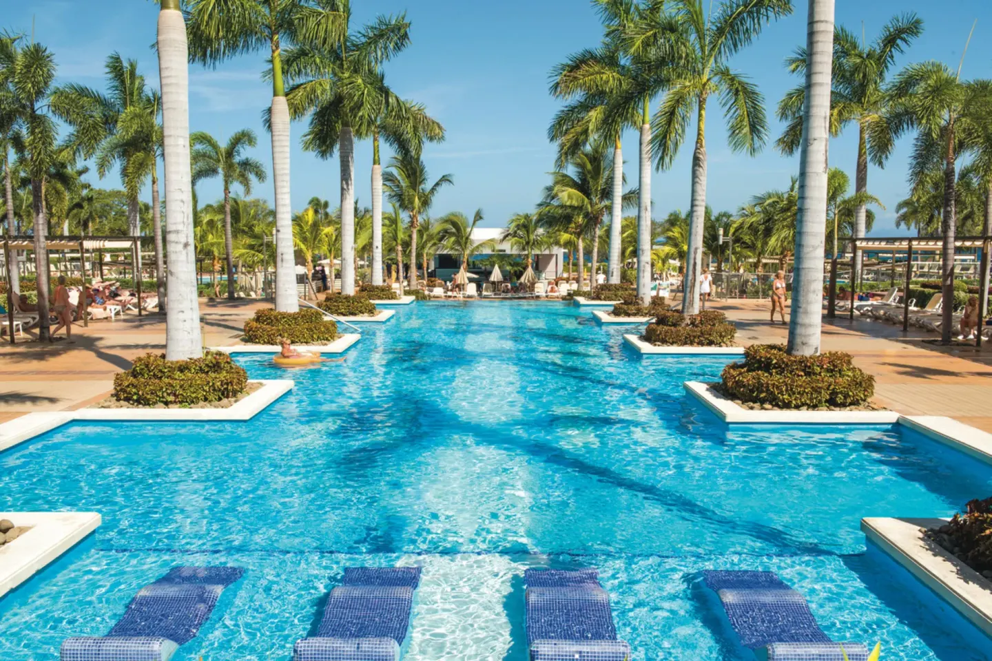 Long palm-lined swimming pool with in-water loungers at Hotel Riu Palace Costa Rica.