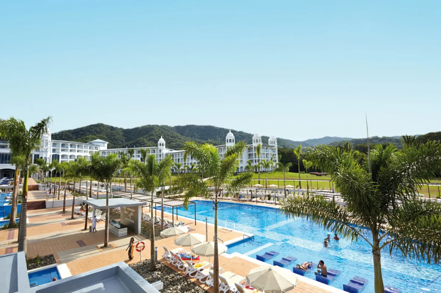 Pool complex, palms, and white resort buildings at Hotel Riu Palace Costa Rica.