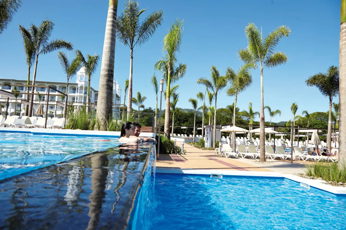 Couple leaning on the raised pool edge at Hotel Riu Palace Costa Rica.