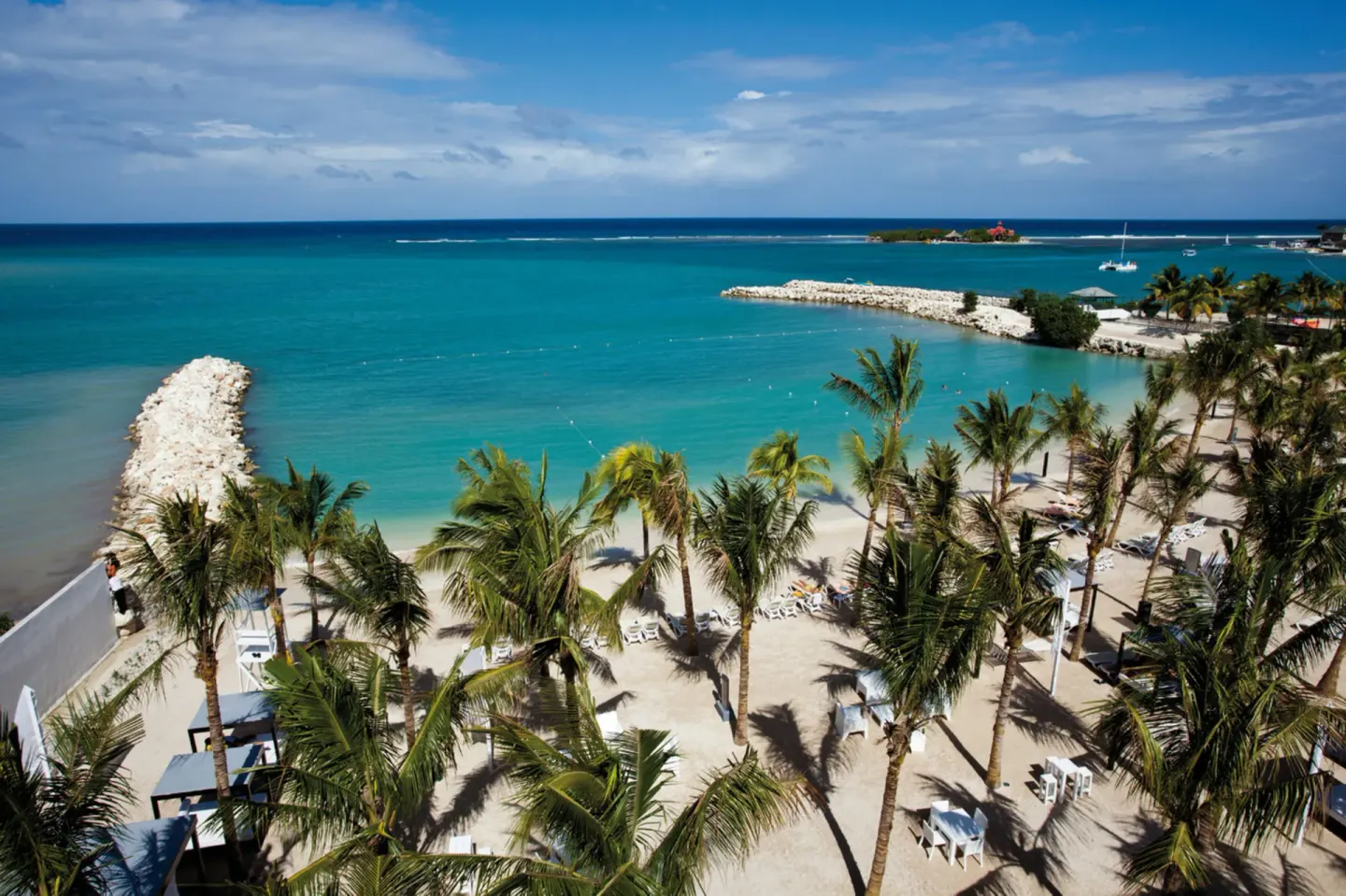 Aerial view of the beach, palm trees, and turquoise bay at Hotel Riu Palace Jamaica.