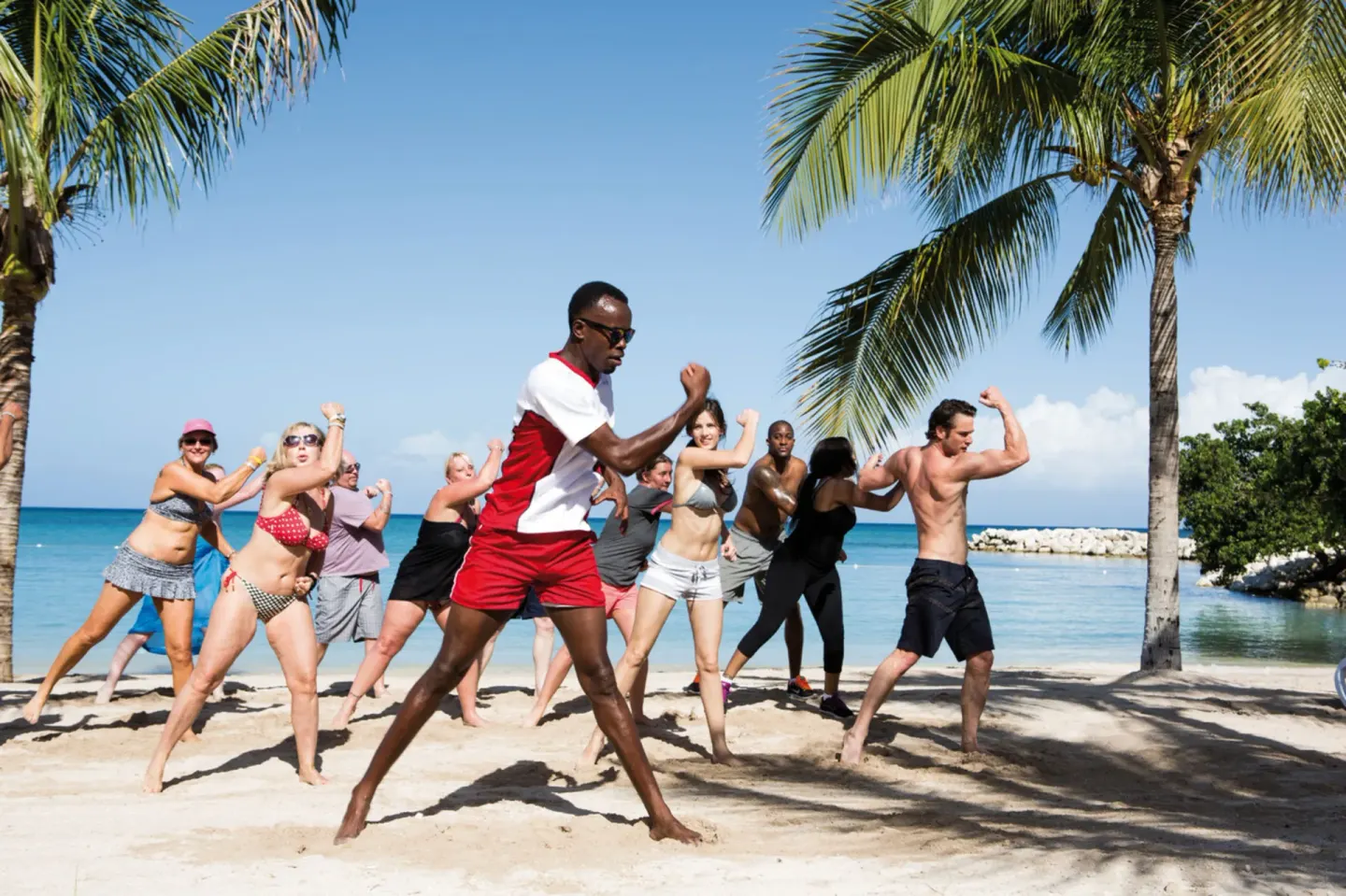 Guests follow a beach fitness class under palm trees at Hotel Riu Palace Jamaica.
