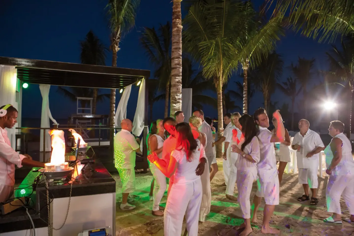 Guests dance on the beach at night near palm trees at Hotel Riu Palace Jamaica.