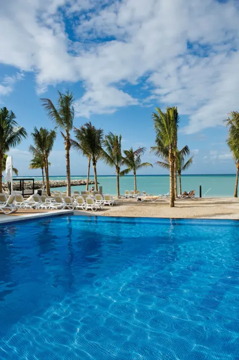 Pool, palm trees, beach loungers, and turquoise sea at Hotel Riu Palace Jamaica.