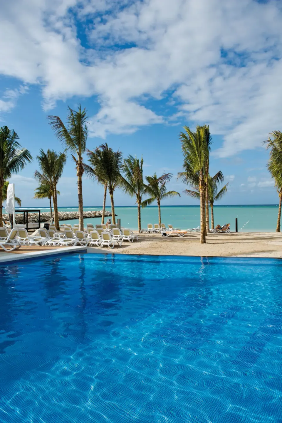 Pool, palm trees, beach loungers, and turquoise sea at Hotel Riu Palace Jamaica.