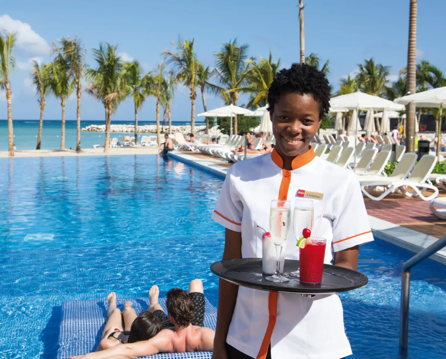 Poolside server carries tropical drinks beside the pool at Hotel Riu Palace Jamaica.