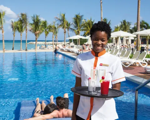 Poolside server carries tropical drinks beside the pool at Hotel Riu Palace Jamaica.