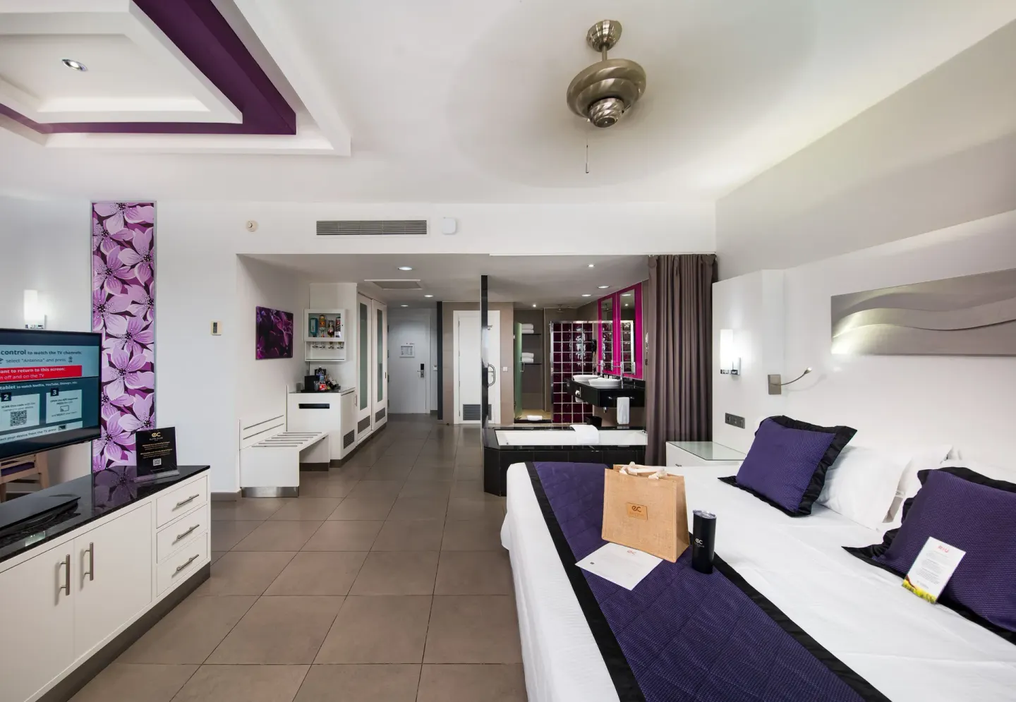 Guest suite with king bed, TV, open bath area, and minibar cabinet at Hotel Riu Palace Jamaica.