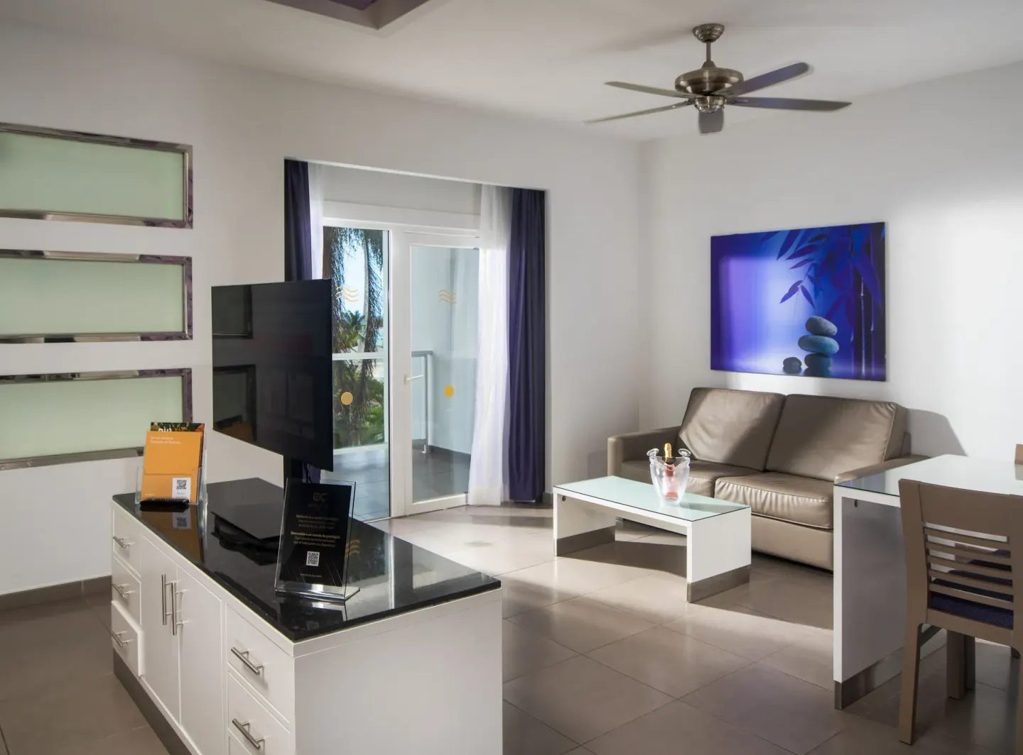 Suite sitting area with sofa, TV, balcony doors, and desk at Hotel Riu Palace Jamaica.