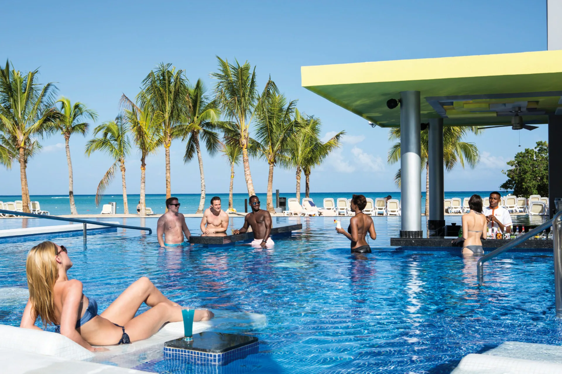 Guests relax in a swim-up pool bar overlooking the beach at Hotel Riu Palace Jamaica.