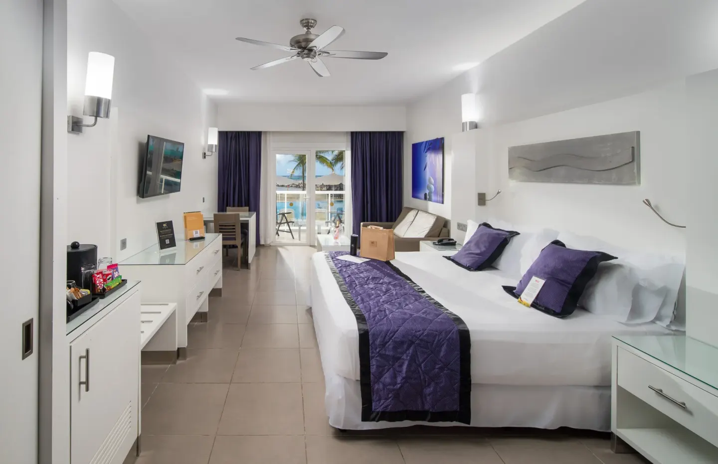 Oceanfront Junior Suite bed, seating area, and balcony doors at Hotel Riu Palace Jamaica.