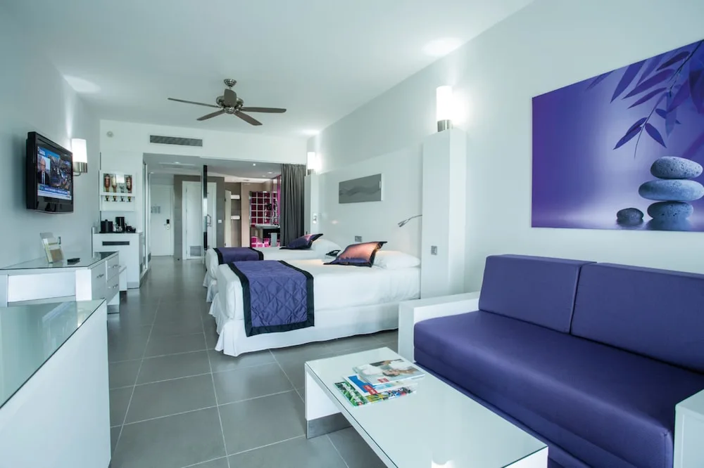 Junior Suite with Garden View room with two beds and purple sofa at Hotel Riu Palace Jamaica.