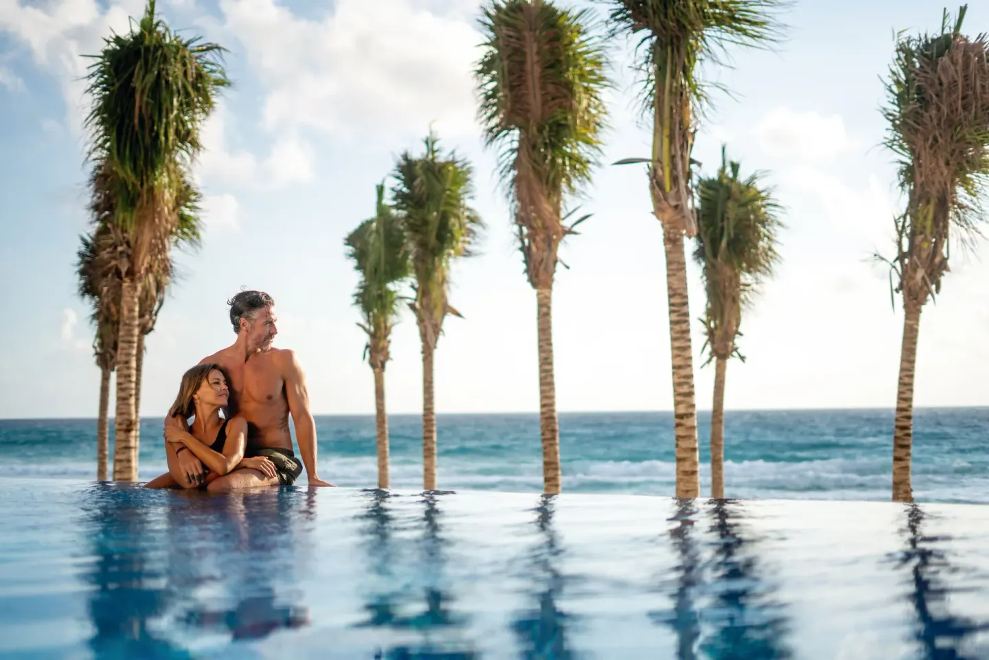 Couple at the infinity pool with ocean and palms at Hotel Riu Palace Kukulkan.