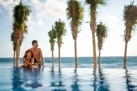 Couple at the infinity pool with ocean and palms at Hotel Riu Palace Kukulkan.