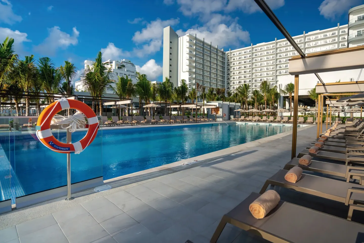 Main pool area with loungers, towels, and hotel building at Hotel Riu Palace Kukulkan.
