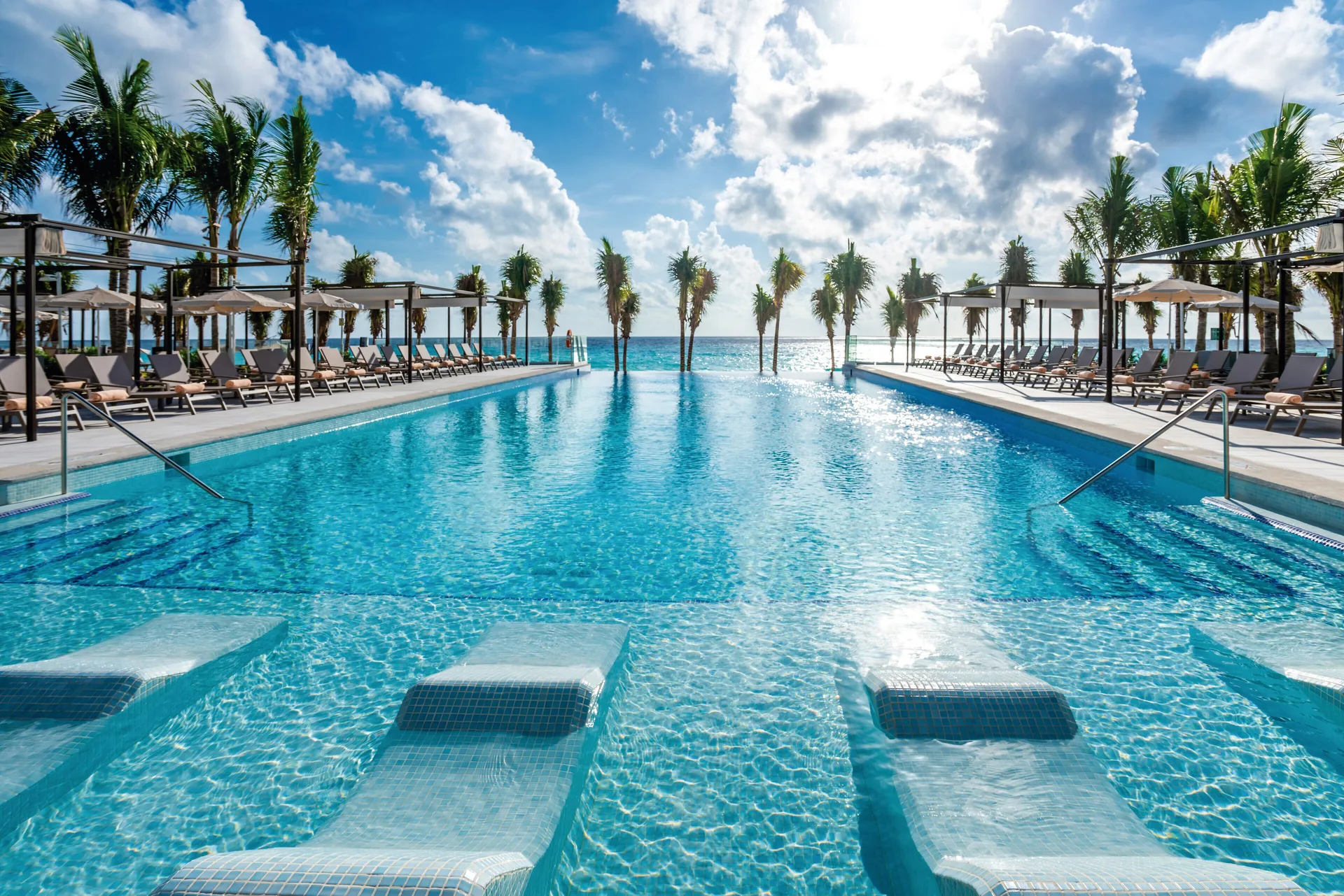 Oceanfront infinity pool with in-water loungers at Hotel Riu Palace Kukulkan.
