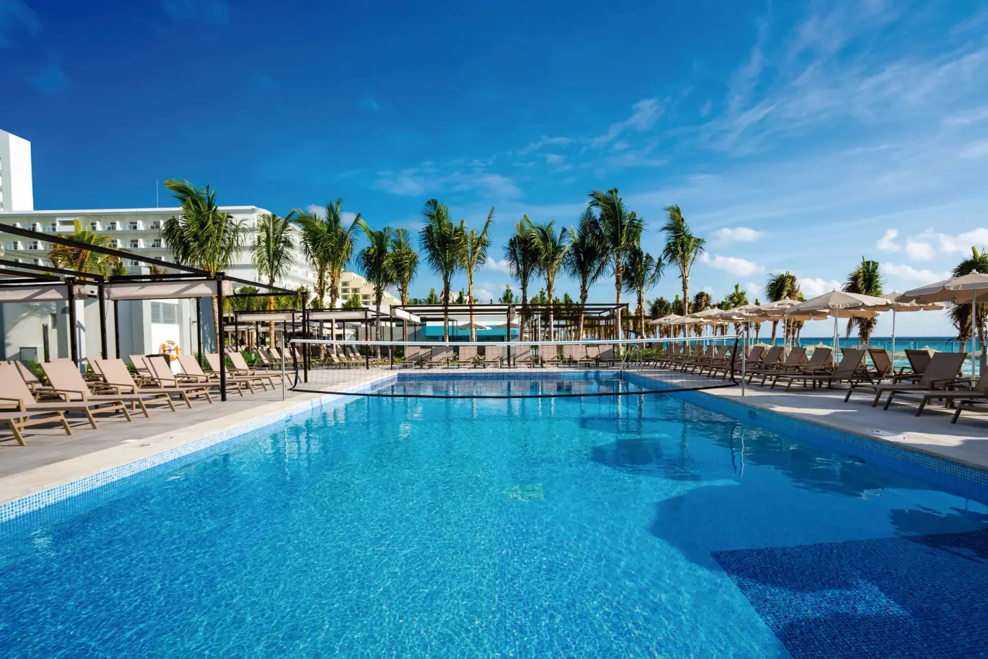 Resort pool lined with lounge chairs and palms at Hotel Riu Palace Kukulkan.